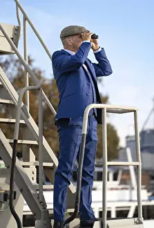 Man with blue suit and hat looking through binoculars