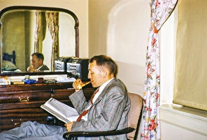 Man in a business suit, smoking a pipe and reading a magazine, sitting in a hotel room, reflected through a mirror, USA around 1953