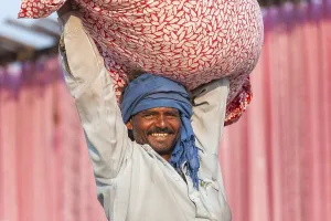 Man carrying a bundle of cloth on his head in front of pink fabric panels