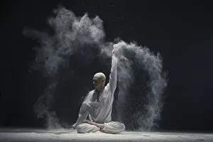 Man doing yoga in white dust cloud in dark room full-length shot