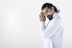 A man dressed in white clasping hands while looking at camera over white background
