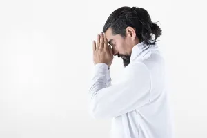 A man dressed in white clasping hands while meditating over white background