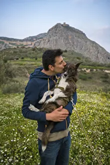 A man lovingly kisses his dog while standing in a lush