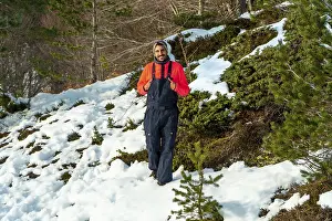 Man in an orange sweater and dark bib pants smiling