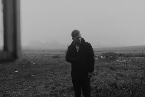 Man in an overcoat standing in a foggy field creates a somber mood