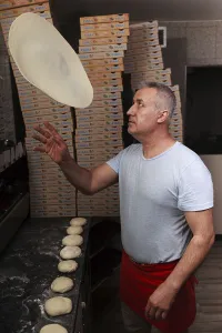 Man, pizza baker, juggles with pizza dough