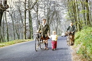 Man riding a bicycle and holding a child by the hand, England, UK, 1956 NB) poor sharpness