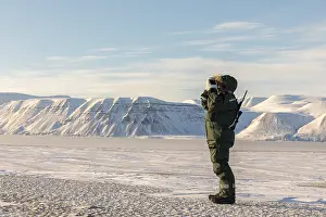 Man with a rifle and binoculars looks out on the horizon in arctic landscape in Billefjorden