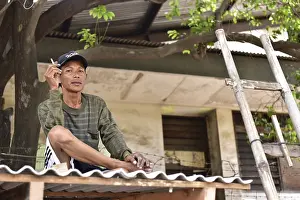 Man sitting relaxed on a roof under a tree smoking a cigarette