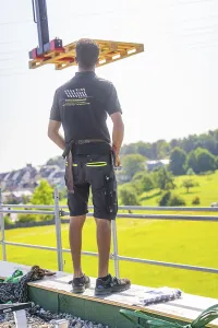 Man stands on a roof and supervises the installation of construction elements with a view of the landscape