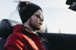 Man in sunglasses and red jacket sits in a convertible