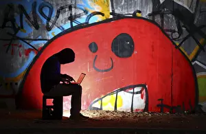Man surfing on a laptop computer in front of a graffiti covered wall