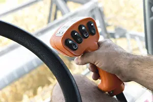 The man's hand holds the control lever of the grain harvester next to the steering wheel<br> The man's hand holds