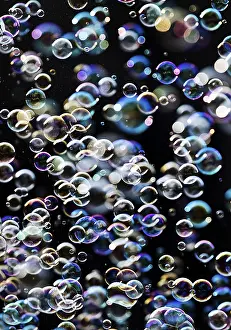 Many, small iridescent and floating soap bubbles against a black background