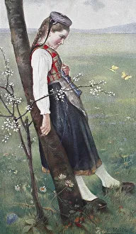 In May, Girl in traditional traditional costume leaning against a tree trunk