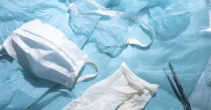 Medical mask and gloves next to goggles on a blue fabric background