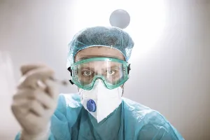 A medical professional in protective gear holding a tool