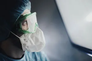 A medical professional in protective gear looking at a bright screen