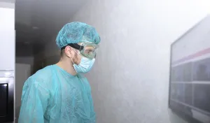 A medical professional in protective gear stands by a wall