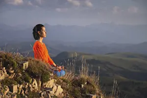 Meditating woman with closed eyes in bright clothes in the mountains