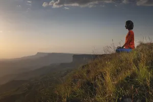 Meditating woman sitting in lotus position near a cliff at sunset overlooking the mountains