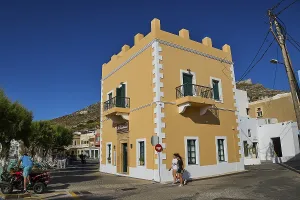 Mediterranean-style corner building with balconies and passers-by under a clear blue sky