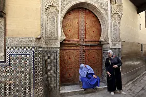 Two men in front of an artfully decorated wooden door with mosaic decoration