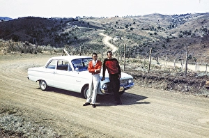 Two men standing next to a Ford Falcon in a hilly landscape in the countryside, Cuba around 1960