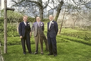 Three men in suits and white carnation buttonholes stand in the garden dressed for a wedding, England, UK 1956