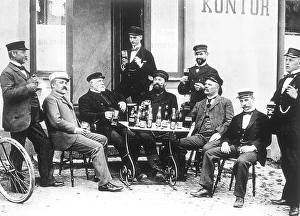 Men's lifestyle in the beginning of the 20th century. A group of men are sitting at a table outside enjoying a glass of beer. They are all three typically well dressed and hats are on. Beer bottles are seen on the table