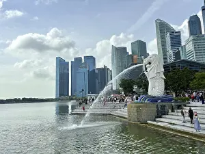 Merlion fountain spouts water in front of the impressive skyline and clouds