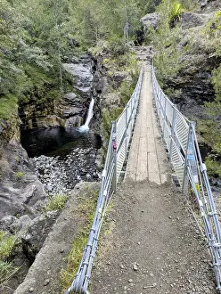 Metal footbridge crossing above a small waterfall in a rocky forested area