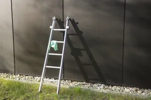 Metal ladder is leaning against a modern building with a cleaning cloth hanging on it