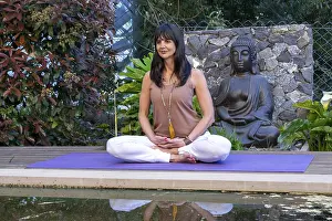 Mid-adult woman meditating outdoors next to a Buddha statue