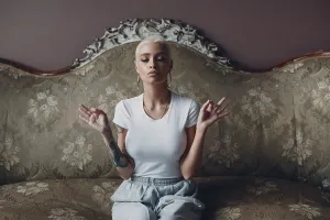 Millenial young woman with short blonde hair portrait sitting and meditate with ok sign mudra on vintage sofa