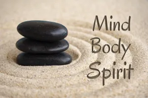 Mind, body and spirit text with black Zen stones on sand background
