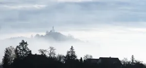 A misty landscape with silhouettes of trees and a chapel on a hill