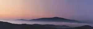 Misty landscape at sunset, mountains rising from clouds of fog in the background