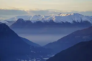Misty valley lies beneath snow-capped mountain peaks at dusk near Piani di Bobbio in Italy