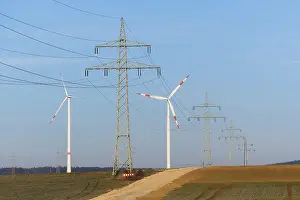 A mix of power lines and wind turbines crosses a country road in a rural setting