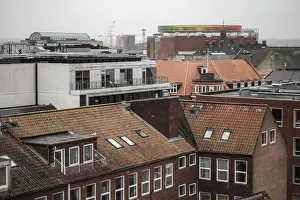 A mix of traditional and modern architecture in a cityscape featuring a colorful rooftop installation in Aarhus