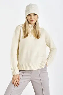 A model stands confidently in a studio while wearing a light sweater and a knitted hat