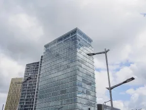 A modern building with a glass facade rises into the cloudy sky