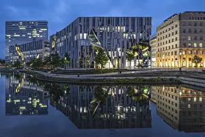 Modern buildings reflected in the water under a blue evening sky