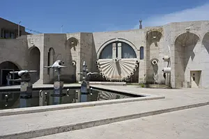 A modern fountain with abstract sculptures surrounded by beige-coloured architecture