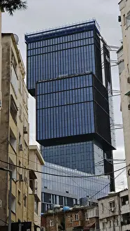 Framed Print : Modern high-rise building with glass facade between older buildings in an urban environment under cloudy sky