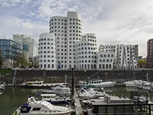 Several modern high-rise buildings and boats in a harbour under a grey sky