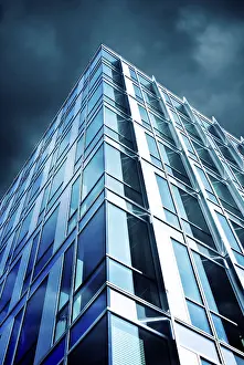 A modern skyscraper with a glass facade reflecting the cloudy sky