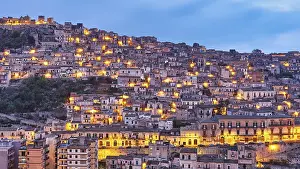 Modica, evening view of a mountainous urban landscape with illuminated houses