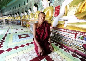 A monk kneeling in front of Buddha statues in a monastery